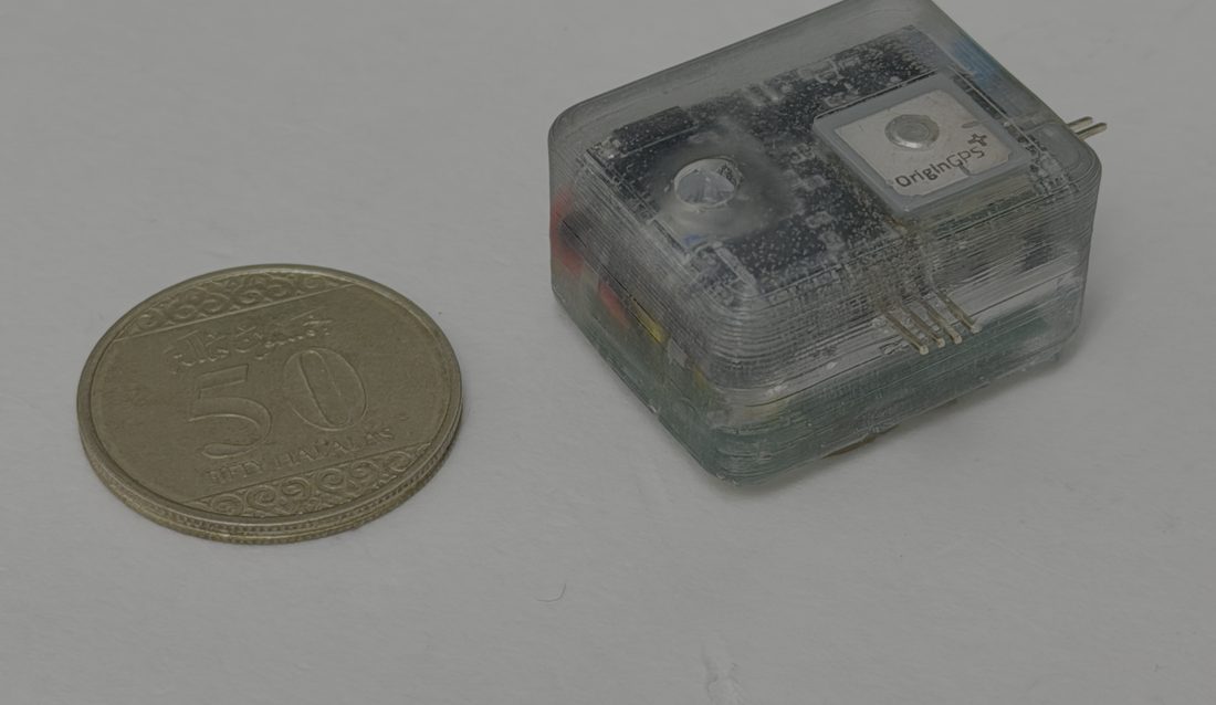 A small transparent tracker with a GPS module beside a coin, for scale